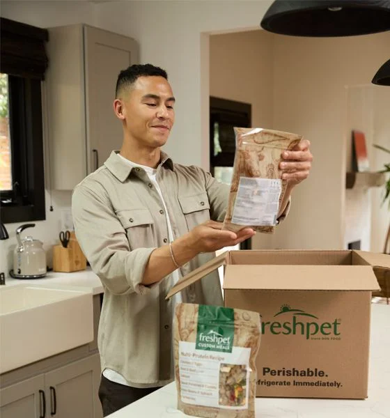 Pet parent unpacking a Freshpet Custom Meals delivery box in his kitchen